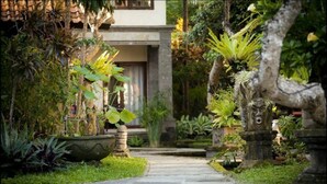 A garden pathway leading to a building with a stone facade, surrounded by lush greenery and a small pond.