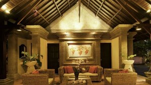 An indoor lounge area with wicker furniture, a framed artwork on the wall, and a tiled floor.