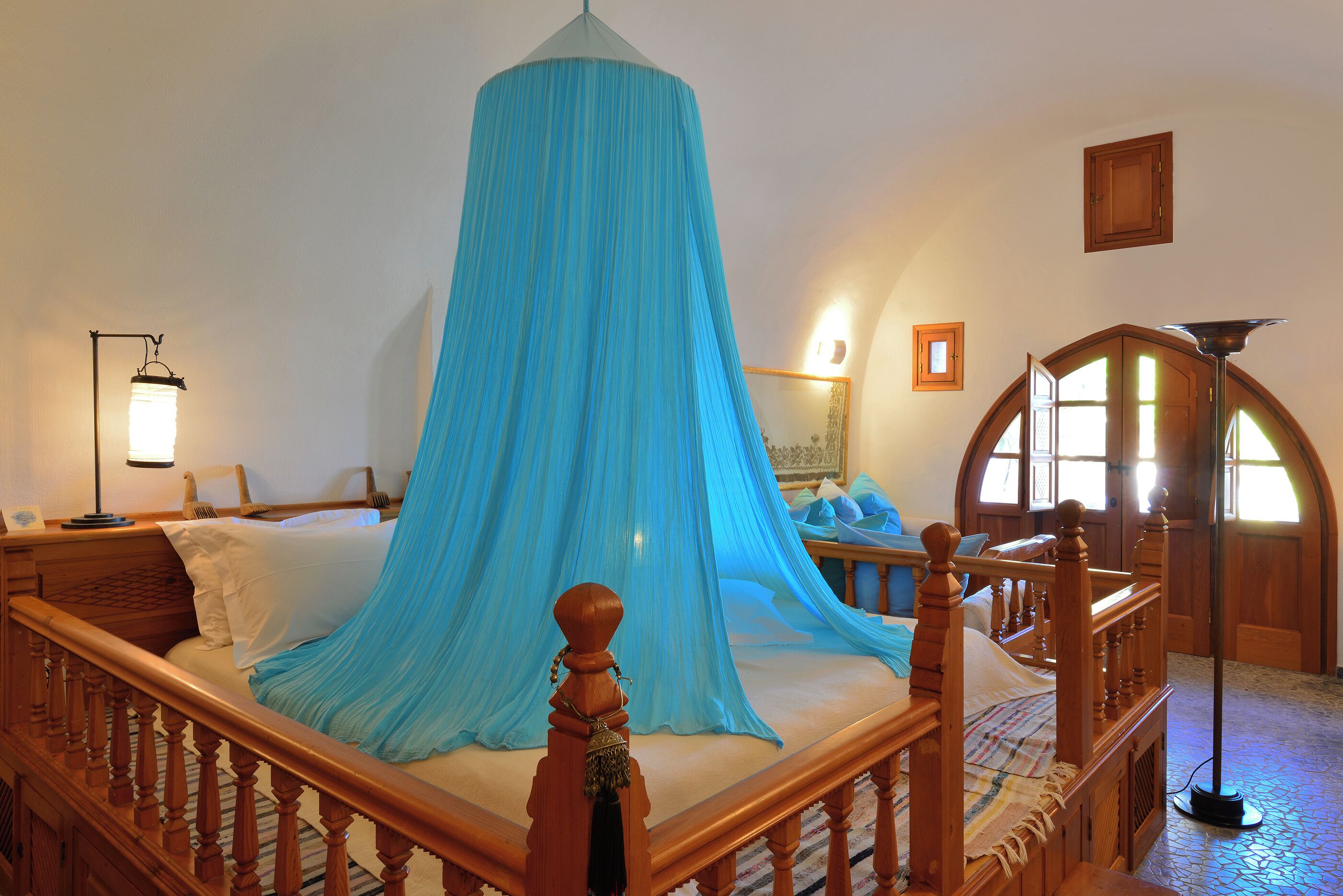 Een bed met een blauw hemelbed, een houten hoofdbord en een nachtkastje met een lamp.