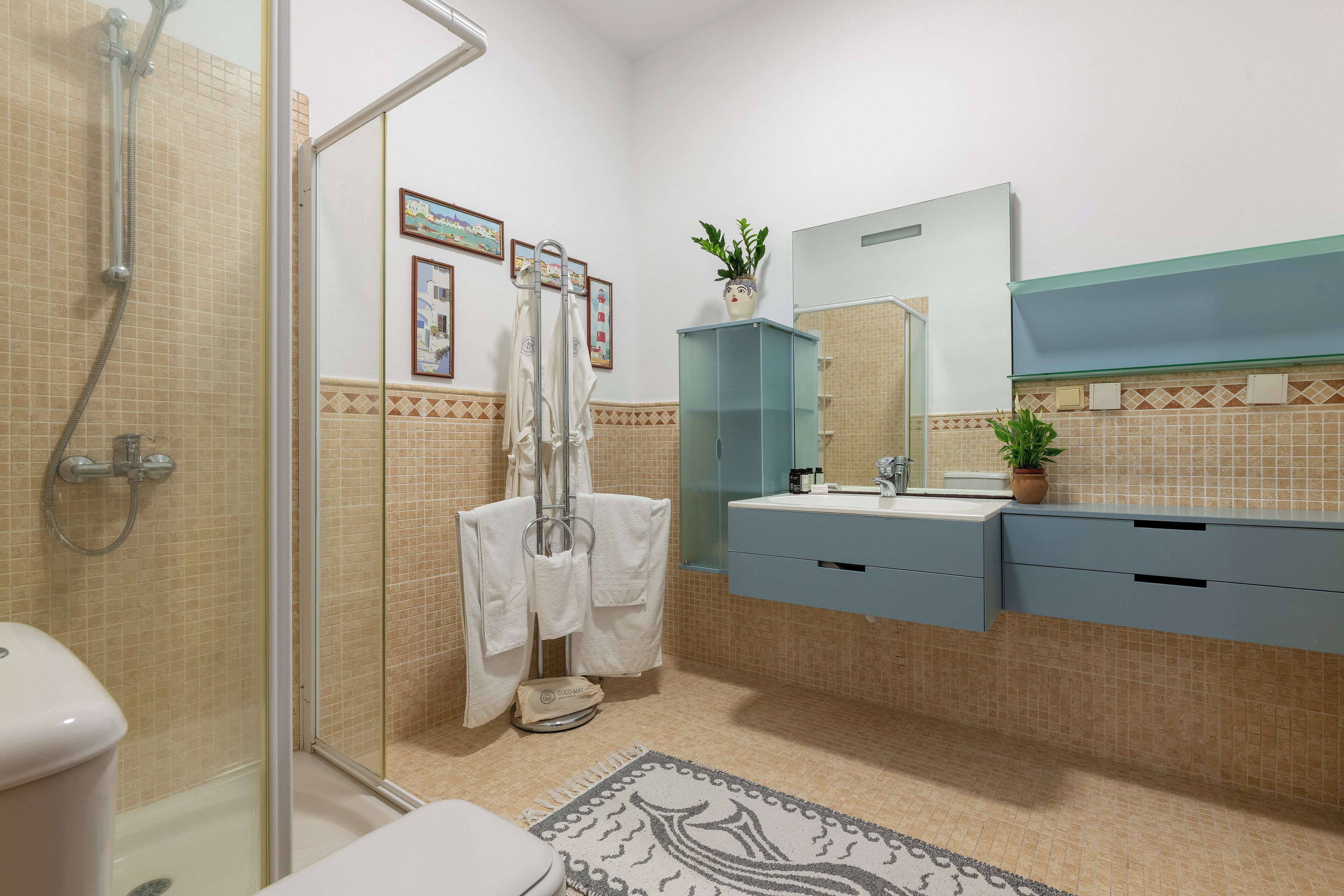 Un baño con cabina de ducha de vidrio, inodoro, lavabo con espejo y un perchero para toallas.