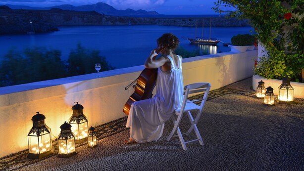 A woman in white sitting on a chair by a waterfront, overlooking a calm sea with boats and a mountainous backdrop. - Melenos Art Boutique Hotel (Rhodes)