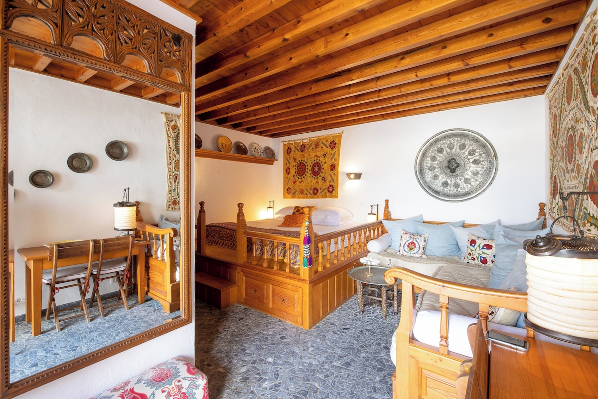 Ein Zimmer mit Holzboden, einem Bett mit Holzüberbau, einer Bank, einem Tisch mit Lampe und einem Spiegel.