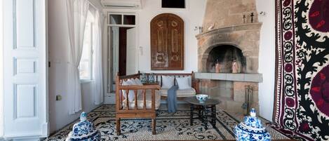 A room with a wooden bench, a fireplace, a patterned rug, and two blue and white vases.