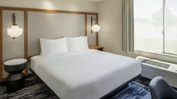 Habitación de hotel con una cama grande, dos mesitas de noche, una silla, un ventanal con vistas y una lámpara en el techo.