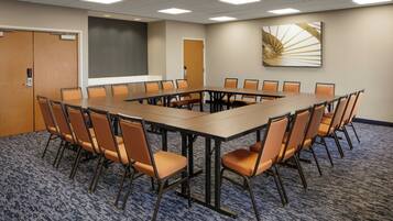 Uma sala de conferências com uma mesa retangular grande rodeada por cadeiras, uma tela de projetor e uma porta.