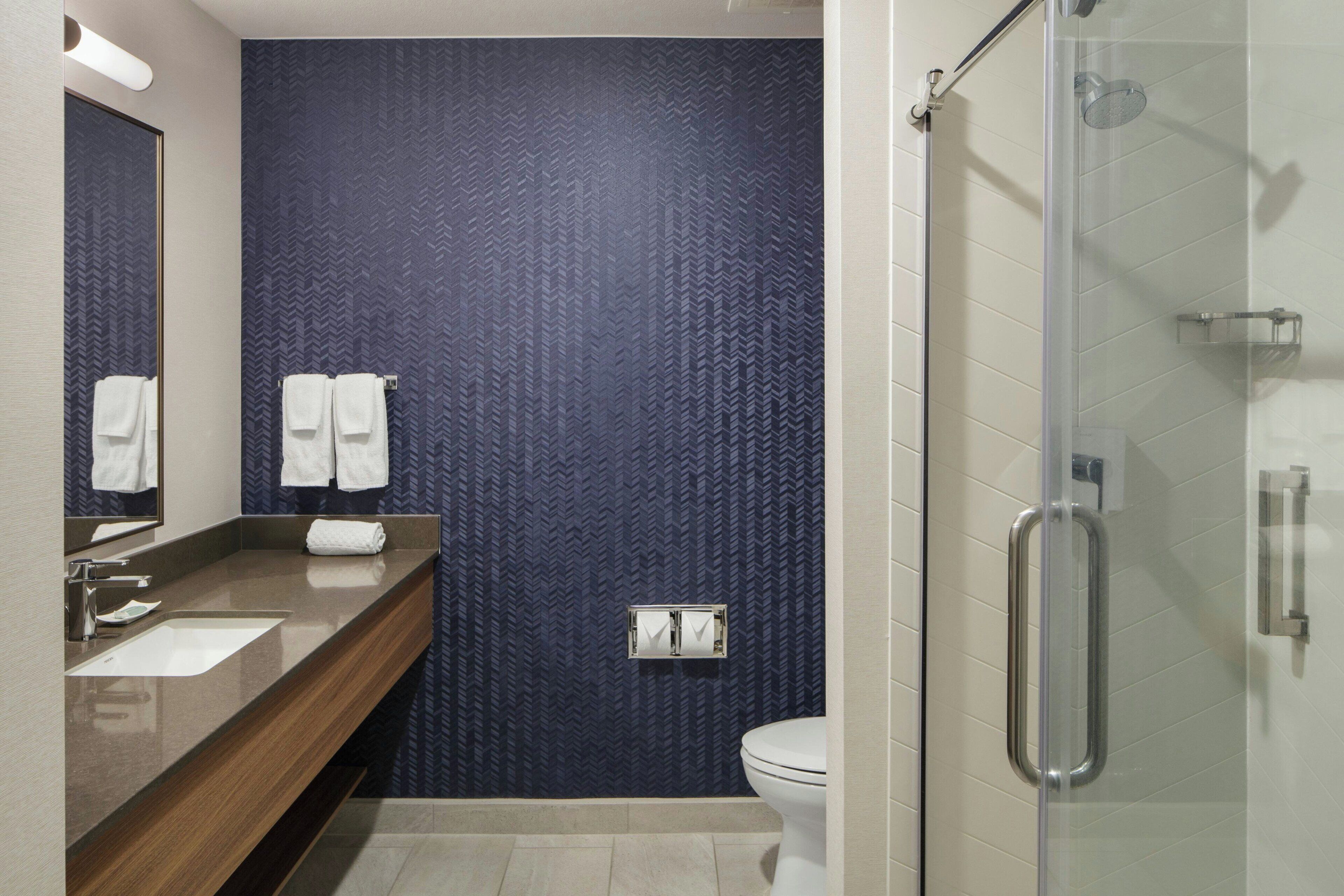 Un baño moderno con una pared de diseño oscuro, un tocador de madera, una cabina de ducha de vidrio y un inodoro blanco.