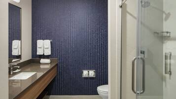 Un baño moderno con una pared de diseño oscuro, un tocador de madera, una cabina de ducha de vidrio y un inodoro blanco.