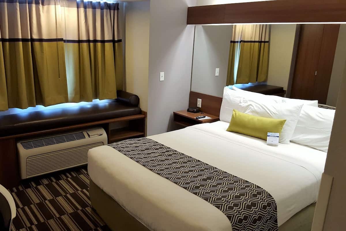 A hotel room with a bed, bedside table, lamp, and a large mirror.