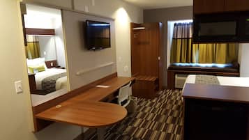 Ein kleines Hotelzimmer mit Bett, Schreibtisch, Stuhl, Fernseher, Mikrowelle und einer kleinen Küchenzeile.