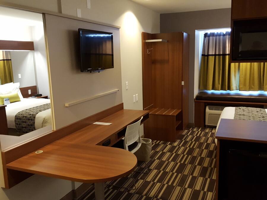 Ein kleines Hotelzimmer mit Bett, Schreibtisch, Stuhl, Fernseher, Mikrowelle und einer kleinen Küchenzeile.
