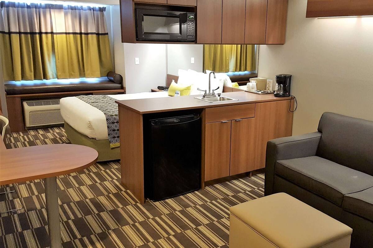 A compact kitchenette with a microwave, sink, and dishwasher. There is a sofa and a small table in the living area.