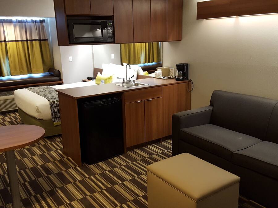 Quarto de hotel compacto com cozinha compacta, um sofá, uma pequena mesa e uma cama com cortinas.