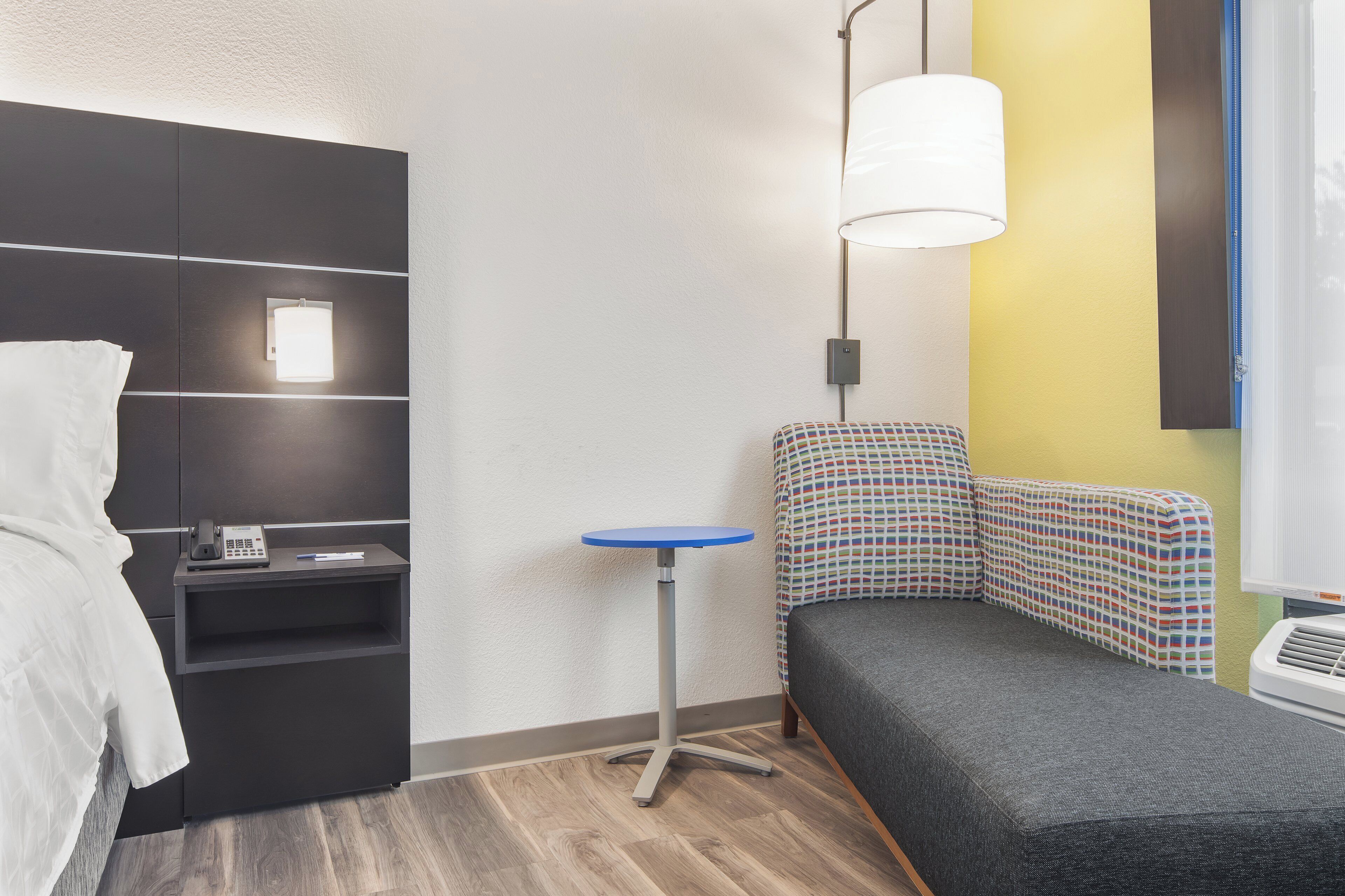 Quarto de hotel moderno com uma cama, uma escrivaninha, uma cadeira e uma mesinha.