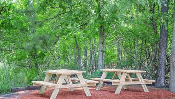 Two wooden picnic tables in a forested area with mulch ground cover.