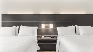 Habitación de hotel con dos camas, una mesita de noche con teléfono y reloj, y una lámpara fijada a la pared.