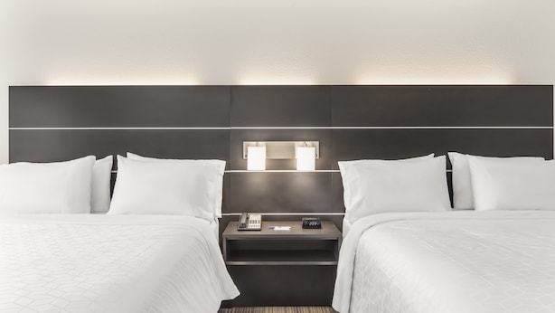 Une chambre d’hôtel avec deux lits, une table de chevet avec un téléphone et une horloge, et un luminaire fixé au mur.