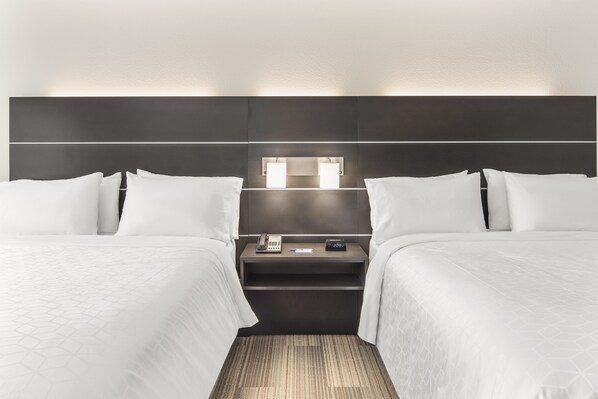 Habitación de hotel con dos camas, una mesita de noche con teléfono y reloj, y una lámpara fijada a la pared.