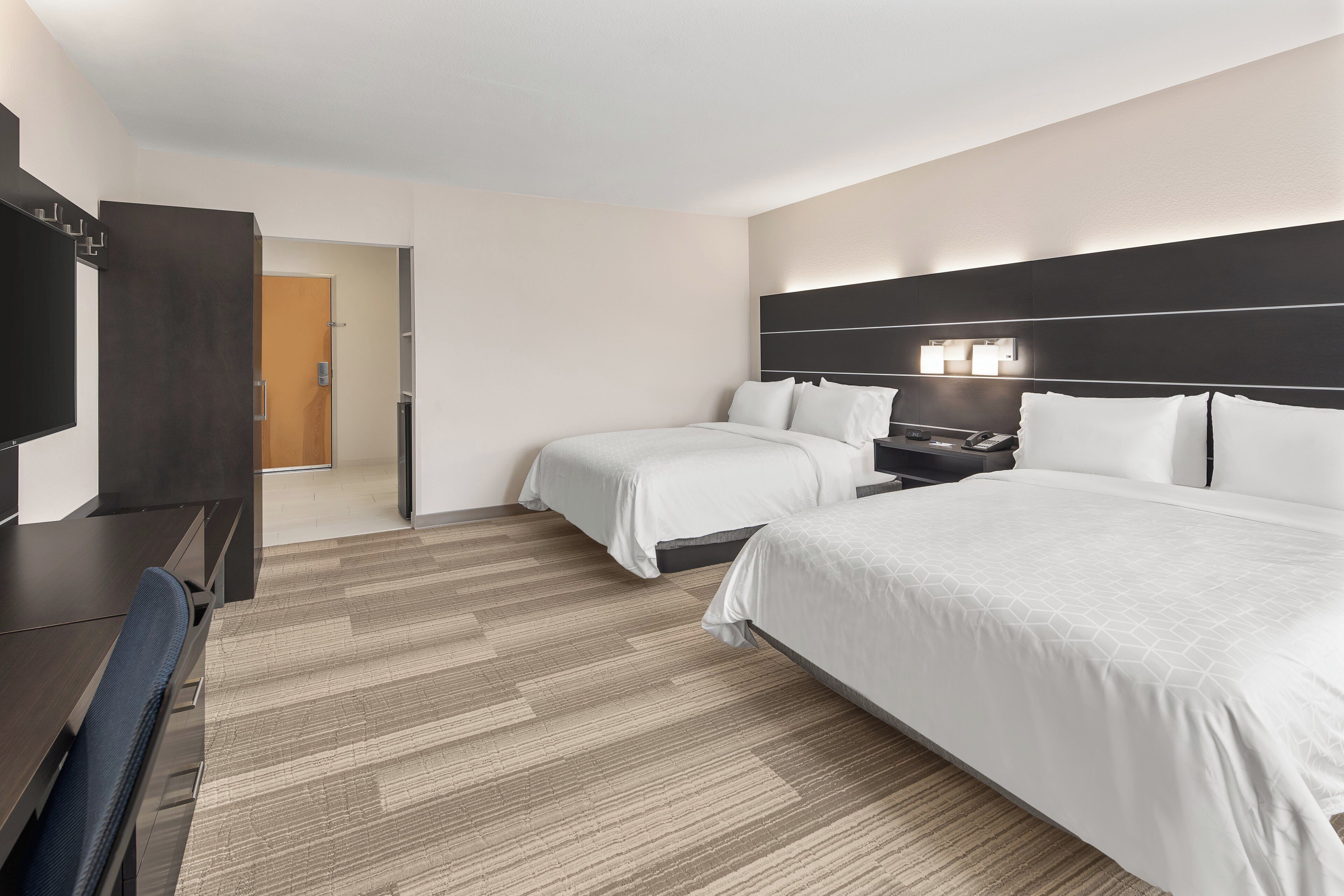 A hotel room with a large bed, a smaller bed, a desk, and a television.