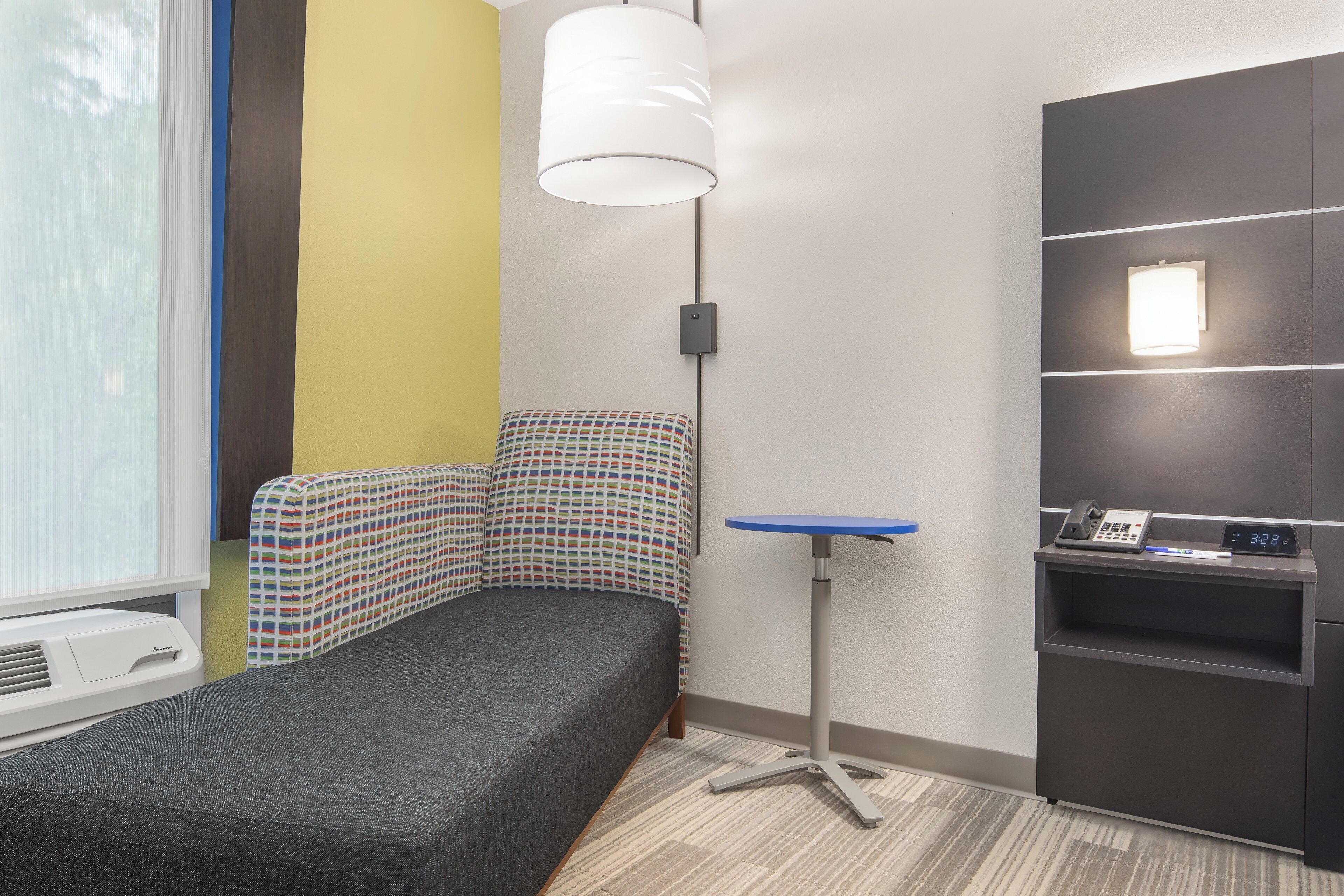 Una stanza piccola e compatta con un letto singolo, una scrivania con un computer e un telefono fissato al muro.