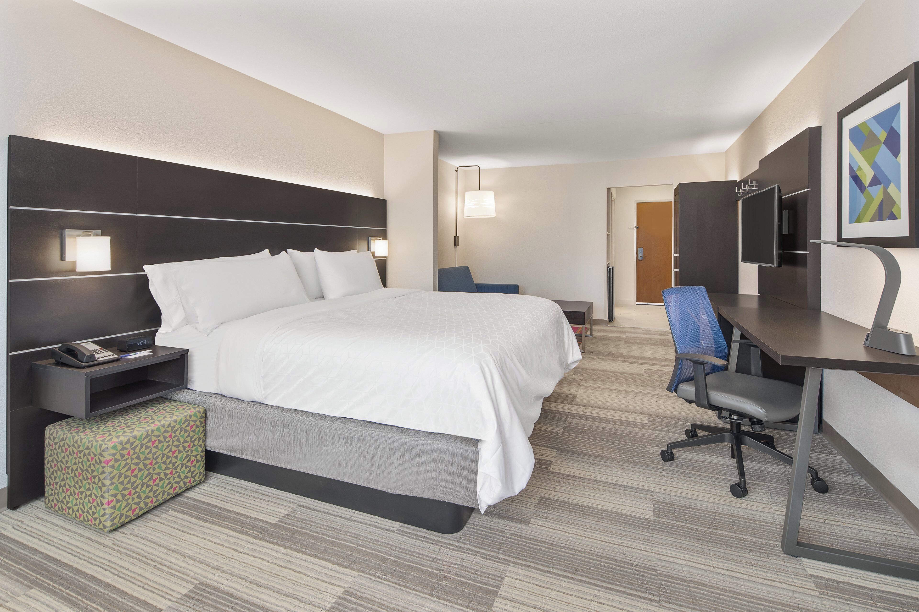 Ein Hotelzimmer mit Bett, Nachttisch, Lampe, Schreibtisch, Stuhl und Fernseher.