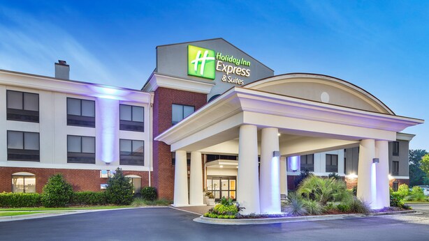 Edificio de Holiday Inn Express & Suites con un letrero llamativo, entrada cubierta y un área frontal ajardinada.