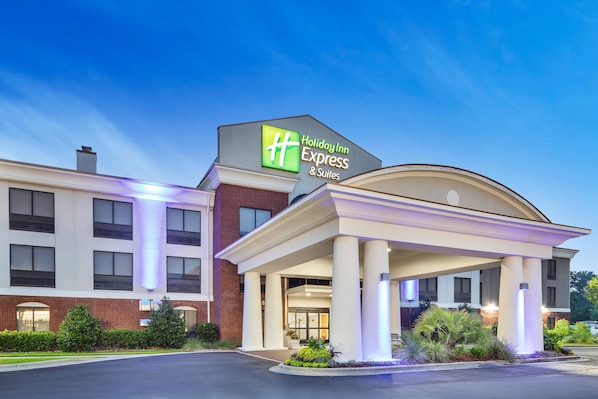 A Holiday Inn Express & Suites building with a prominent sign, a covered entrance, and a landscaped front area.