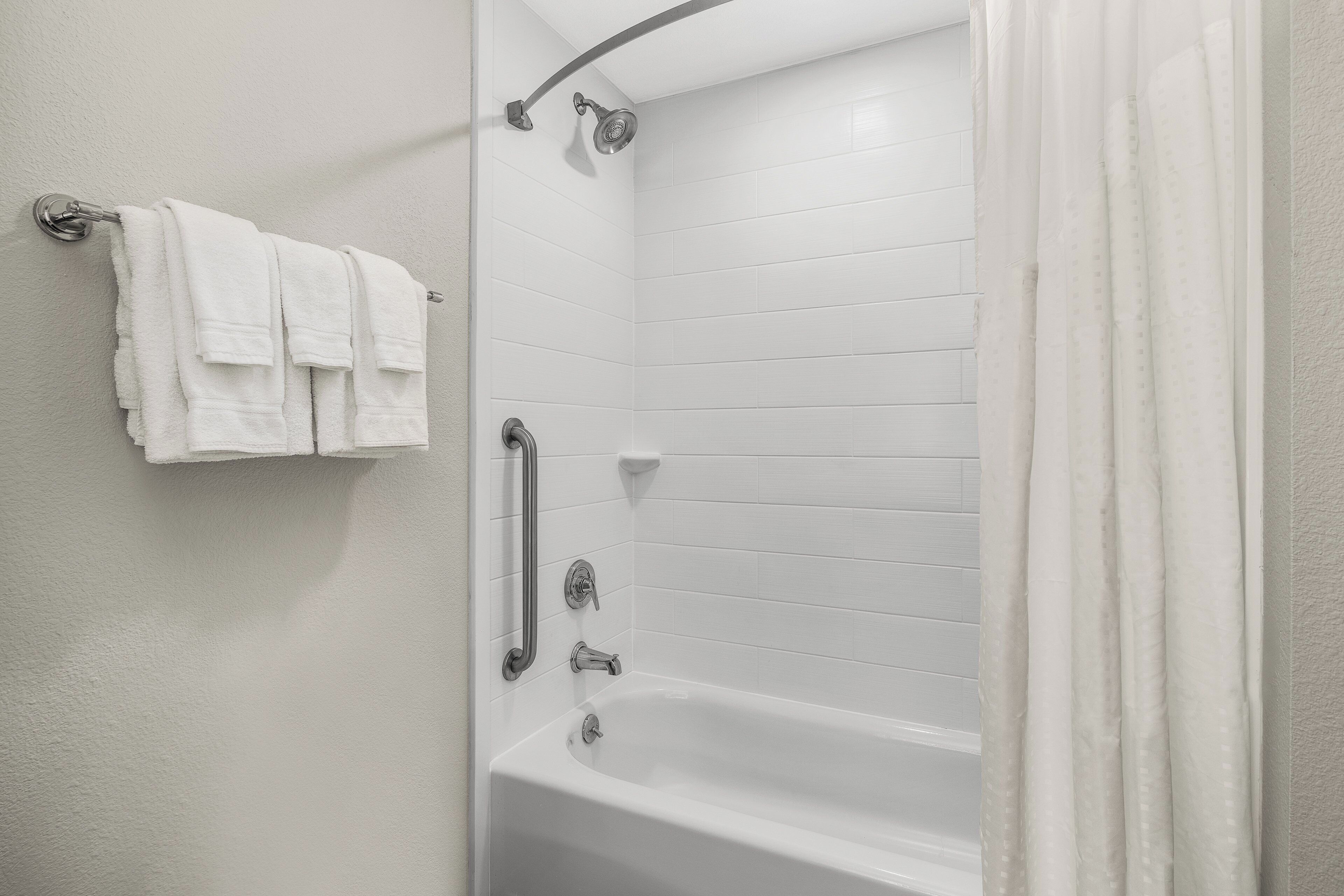 A bathroom with a bathtub, a shower, and a handrail.