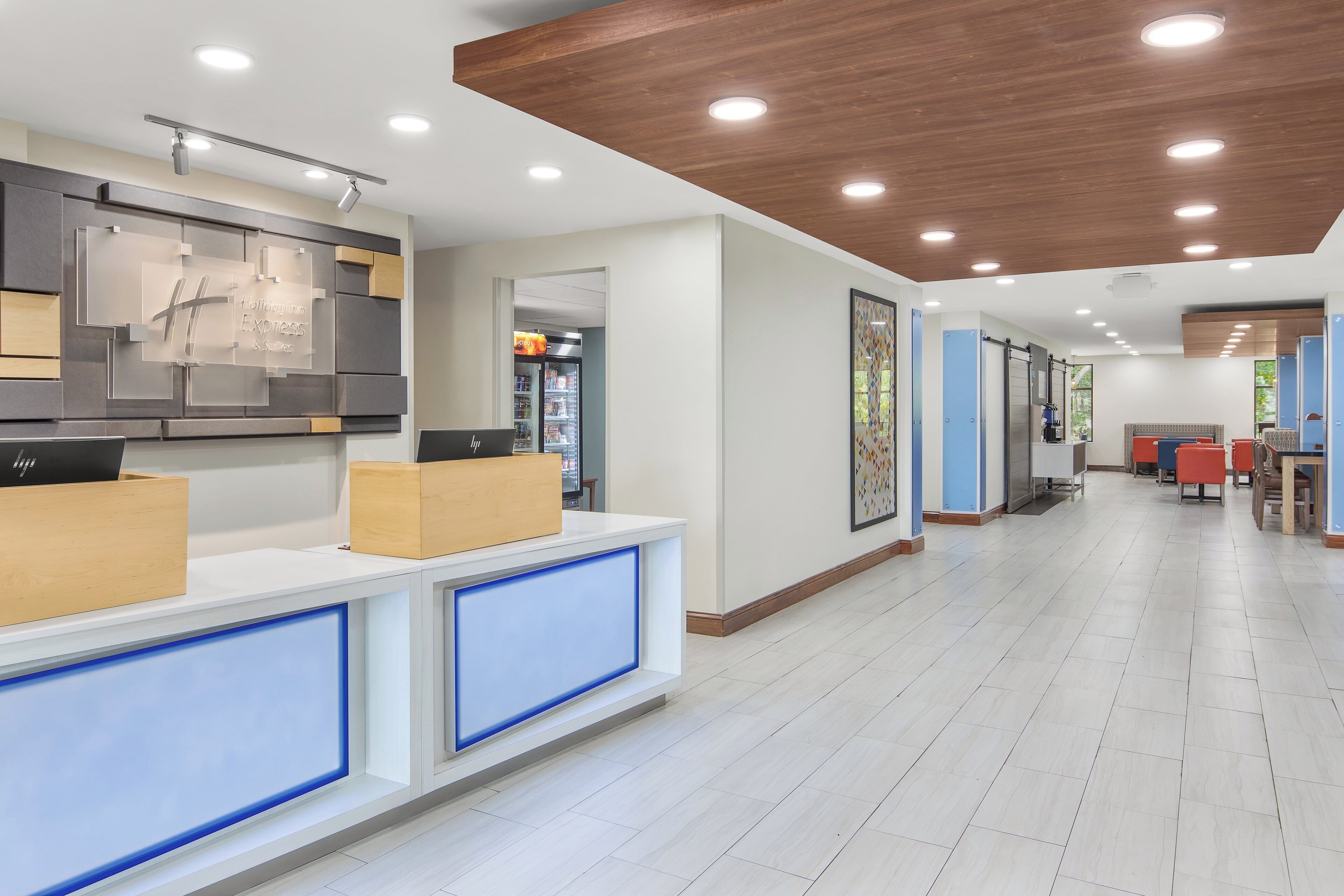 A hotel reception area with a modern design, including a reception desk, a refrigerator, and a seating area with chairs and tables.