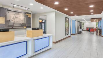 A hotel reception area with a modern design, including a reception desk, a refrigerator, and a seating area with chairs and tables.