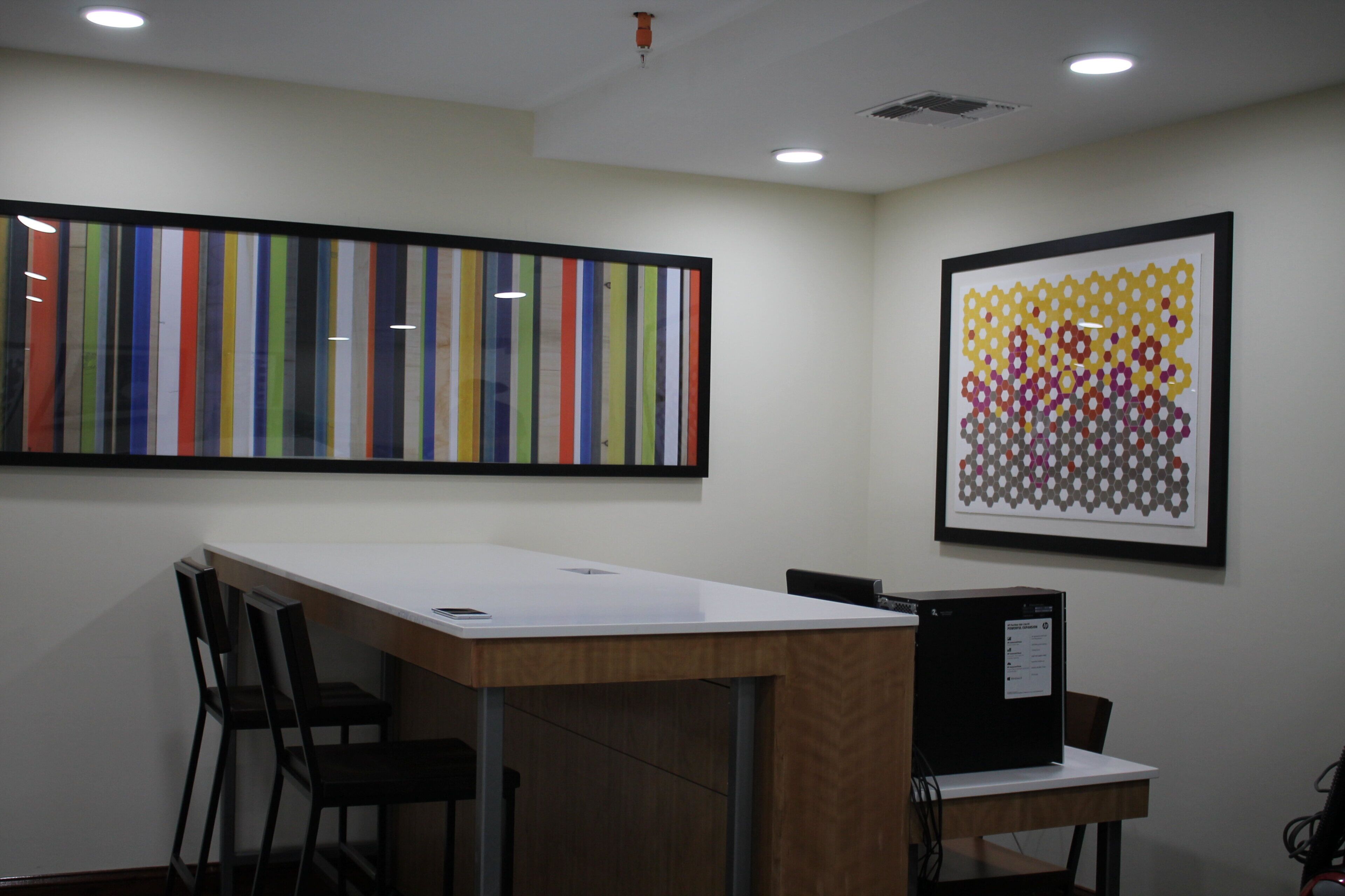 A conference room with a long table, chairs, a projector, and two framed artworks on the walls.