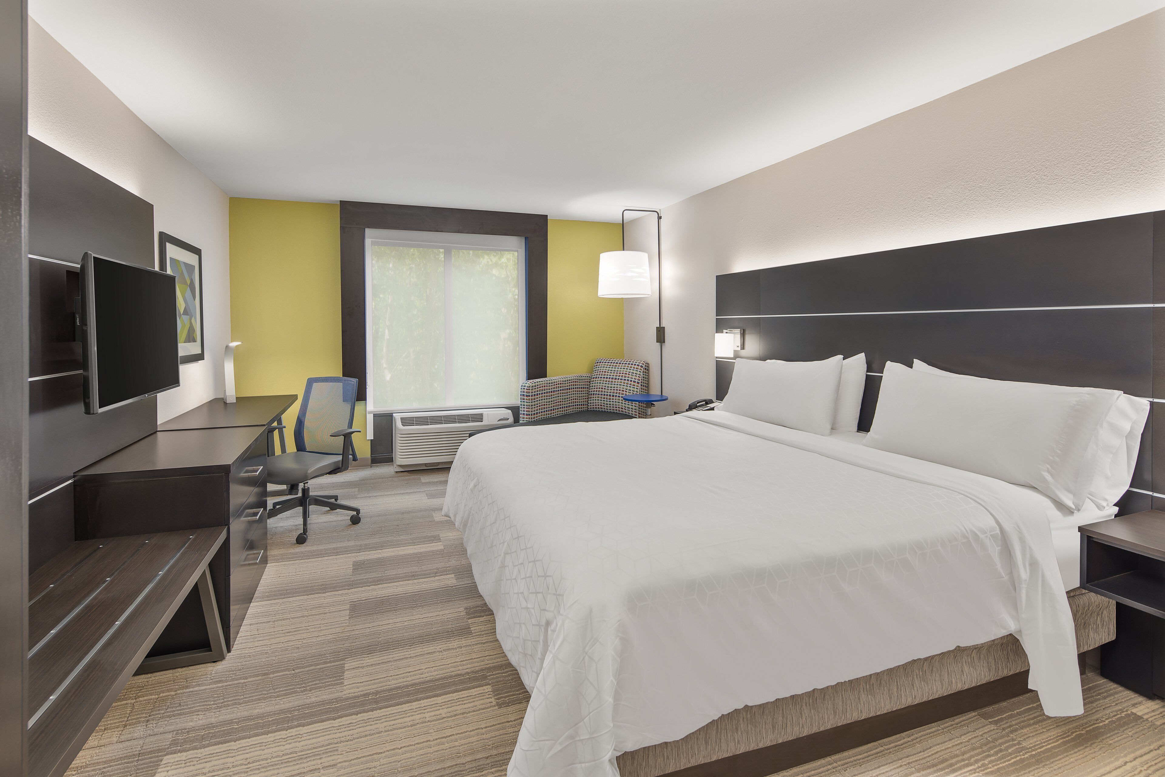 Una habitación de hotel con una cama grande, un escritorio con silla, un televisor de pantalla plana y una ventana con persianas.