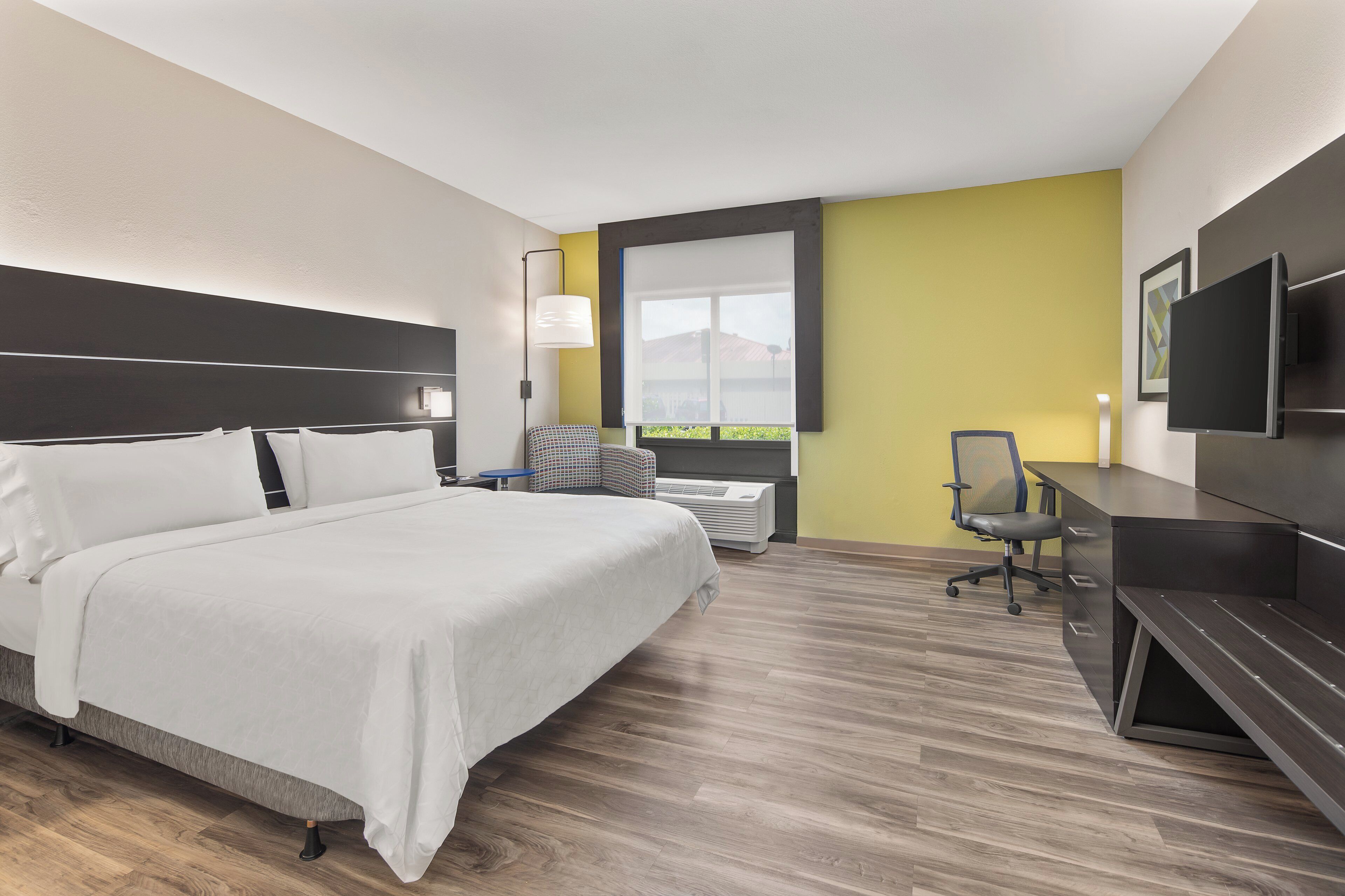 A hotel room with a bed, desk, chair, TV, and a window with a view.