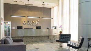Ein Hotel-Empfangsbereich mit Marmorboden, einem grauen Sofa, einem schwarzen, mit Wirbeln verzierten Sessel und einer Rezeption mit dem Schild "GOINN HOTEL".