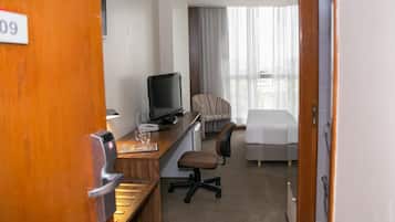 Et hotelværelse med skrivebord, computer, stol, seng og udsigt til det fri.