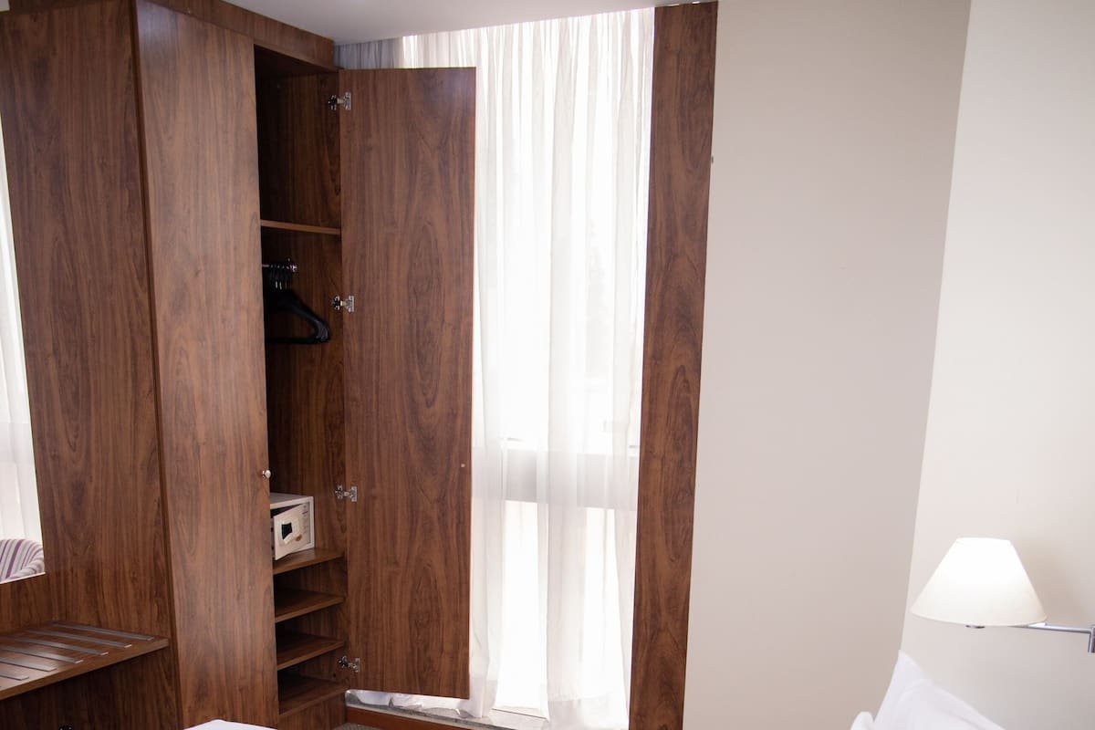 Habitación de hotel con una cama grande, armario de madera y una ventana con cortinas.