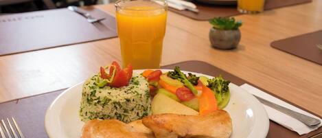 Un plato de comida con arroz, verduras y pollo, un vaso de jugo de naranja y un tenedor sobre una mesa.
