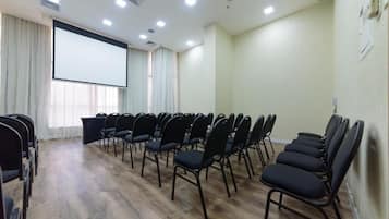 A conference room with rows of black chairs, a large projection screen, and a wooden floor.