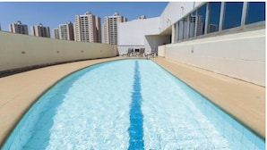 Ein Swimmingpool mit blauer Fahrspurmarkierung, umgeben von einer beigefarbenen Liegefläche und einer weißen Wand.