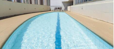 A swimming pool with a blue lane marking, surrounded by a beige deck and a white wall.