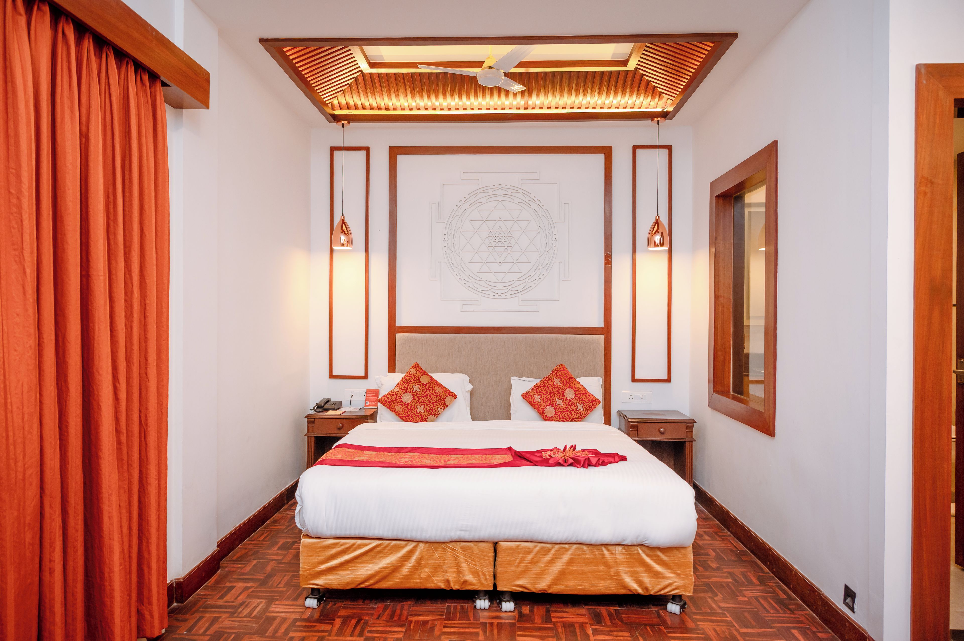 Una habitación de hotel con una cama, un ventilador de techo, una obra de arte en la pared y piso de madera.