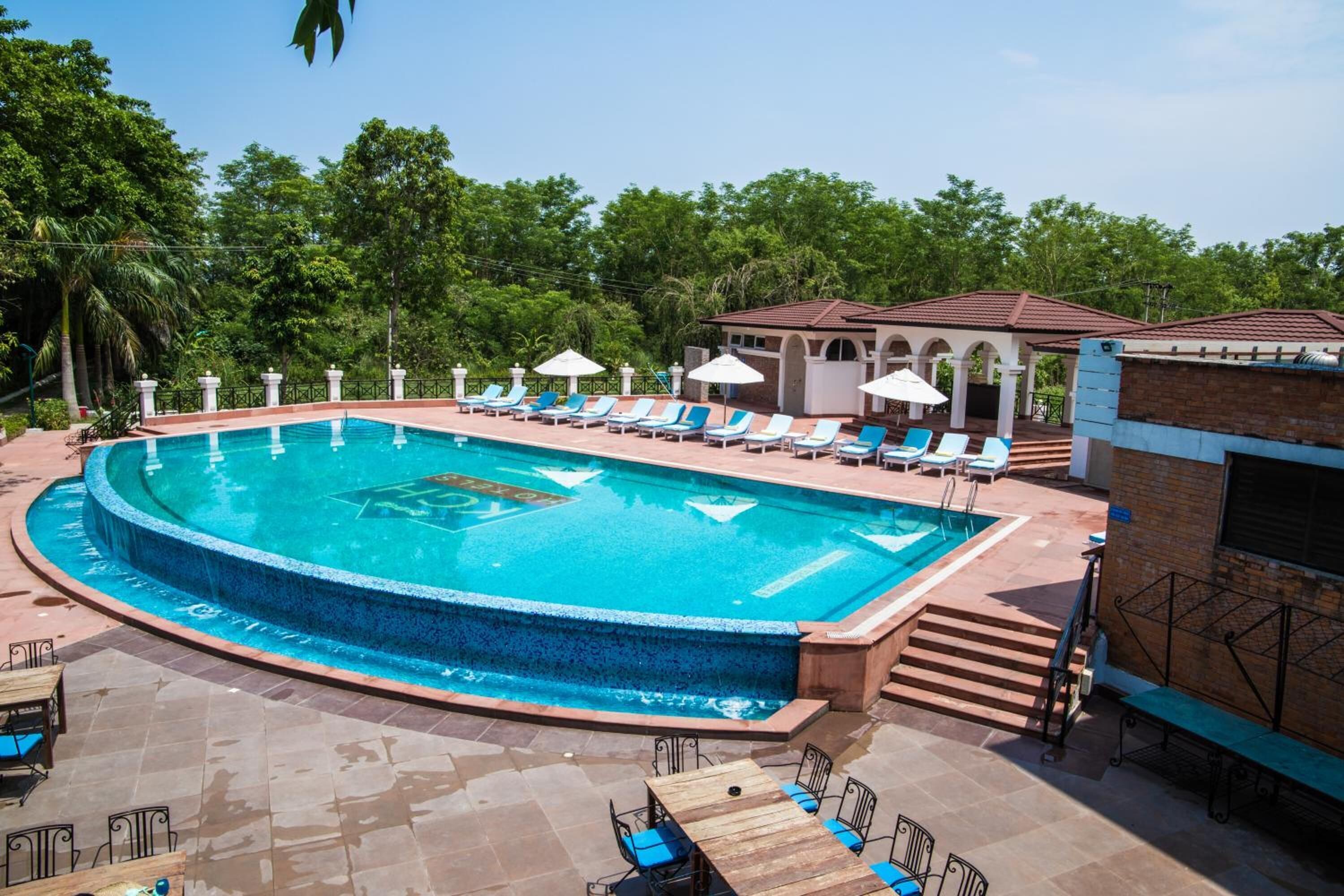 Ein Swimmingpool mit Liegestühlen und Sonnenschirmen, umgeben von Grünpflanzen und einem Gebäude mit Ziegeldach.