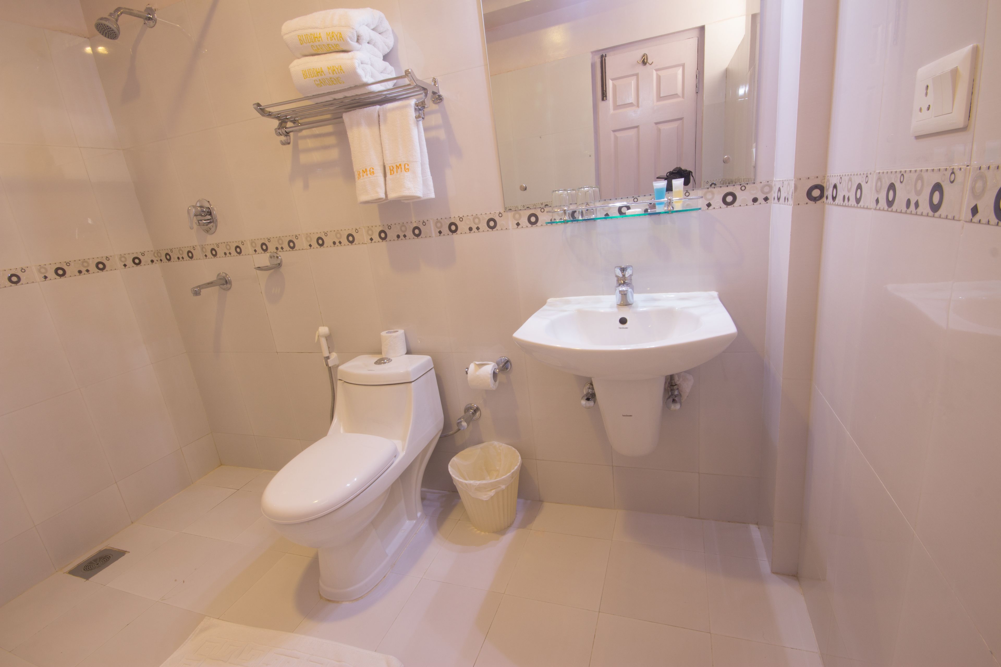 A bathroom with a toilet, sink, and shower. There are towels hanging on a rack and a trash can.