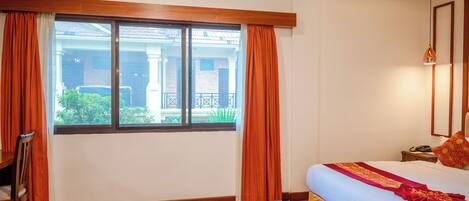 A hotel room with a large window, wooden flooring, a bed with a red and white bedspread, and a nightstand with a phone.