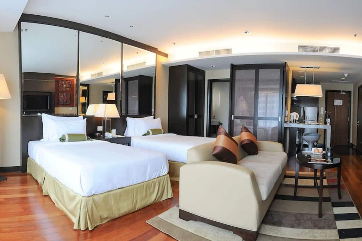 A hotel room with two beds, a sofa, a TV, and a minibar.