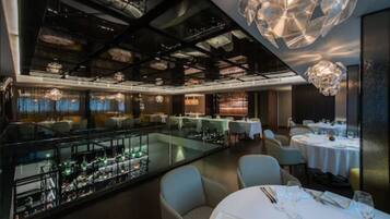 Un restaurante moderno con techo alto, barandillas de vidrio y luminarias contemporáneas.
