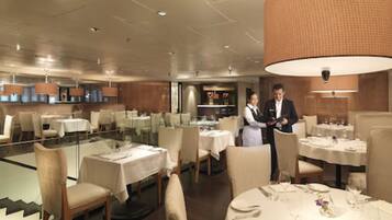 A modern dining area with round tables, chairs, and a large hanging light fixture.