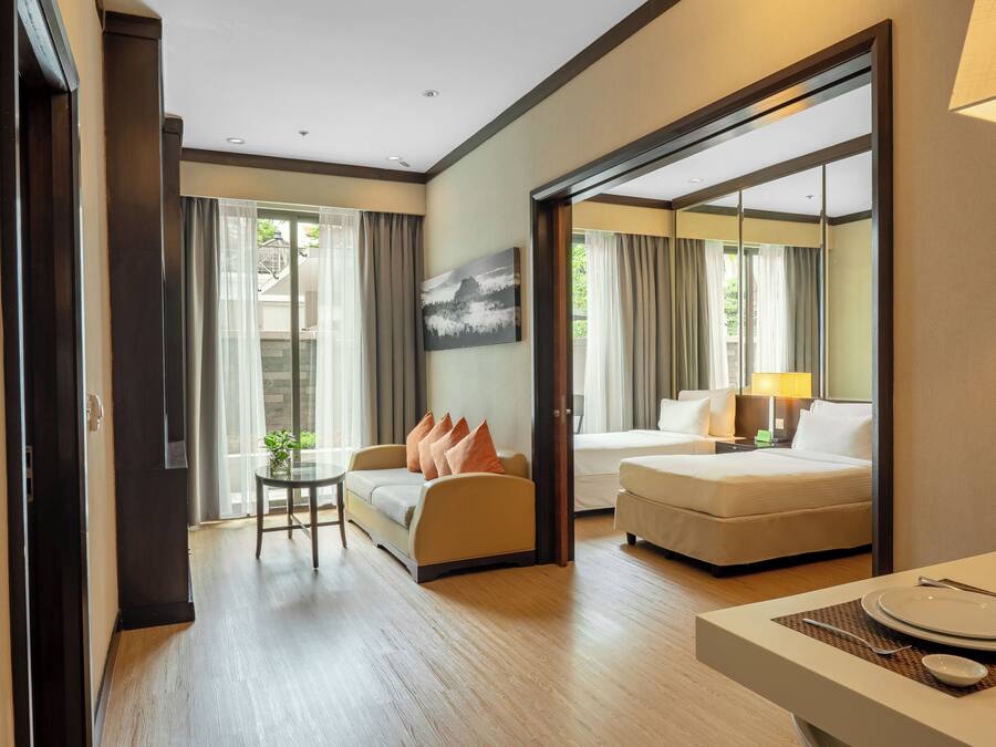 A hotel room with a sofa, a dining table with plates, a lamp, and a painting on the wall.