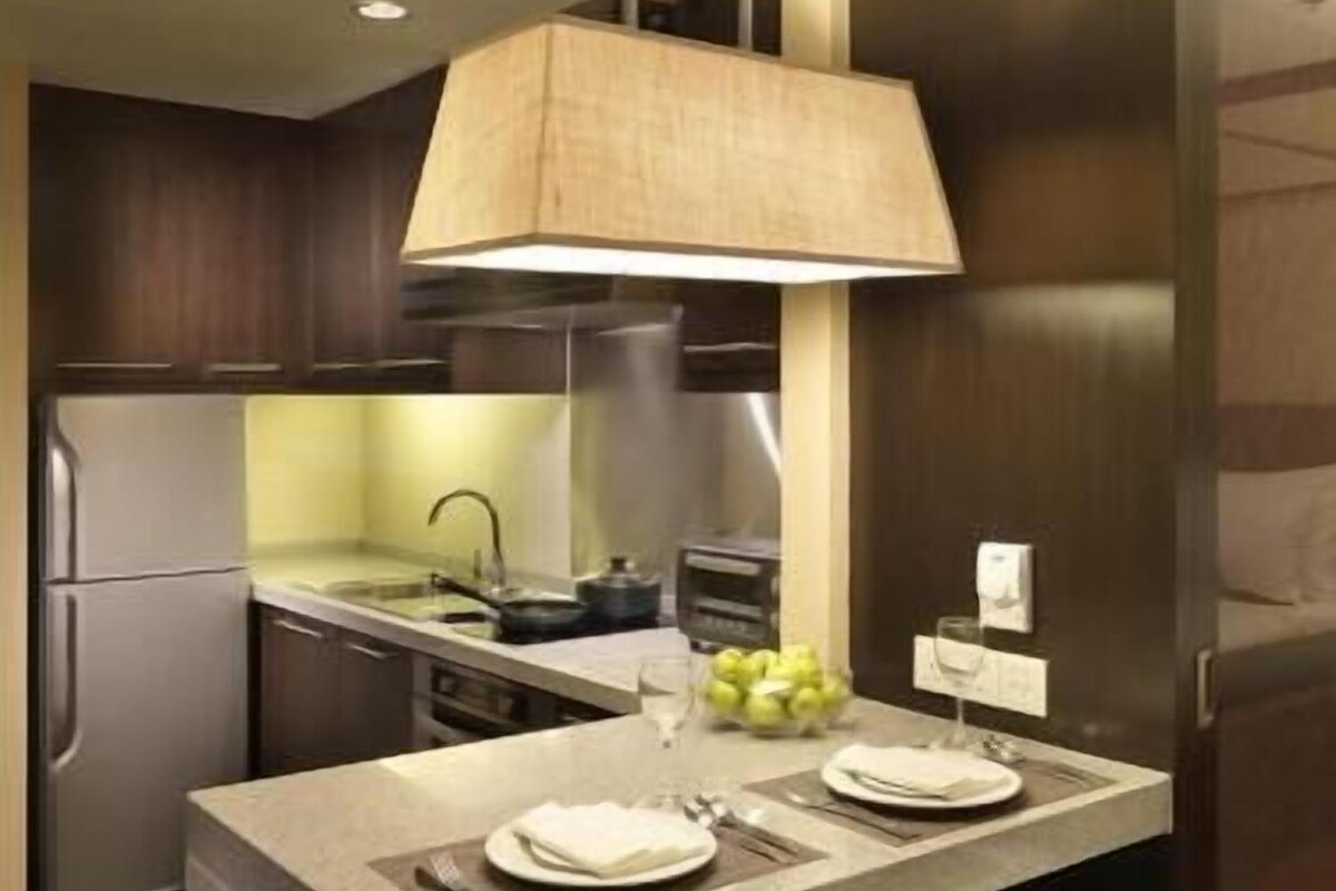 A modern kitchen with a central island, bar stools, a hanging light fixture, and stainless steel appliances.