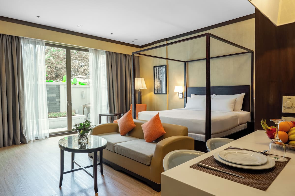 A hotel room with a four-poster bed, a sofa, a dining table set for two, and a view through the glass door.