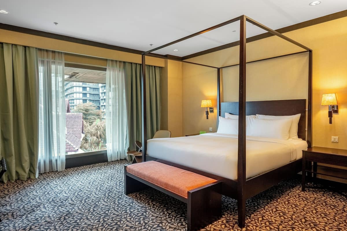 A four-poster bed with a bench, a desk, and two lamps.